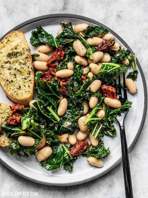 Sun Dried Tomato, Kale, and White Bean Skillet on a plate with slices of rustic bread